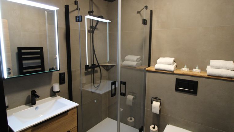 Ein modernes Badezimmer mit einer gläsernen Dusche und eleganten Armaturen. Auf dem Waschbecken liegt ein Handtuch bereit, und der Raum ist mit neutralen Farben gestaltet.