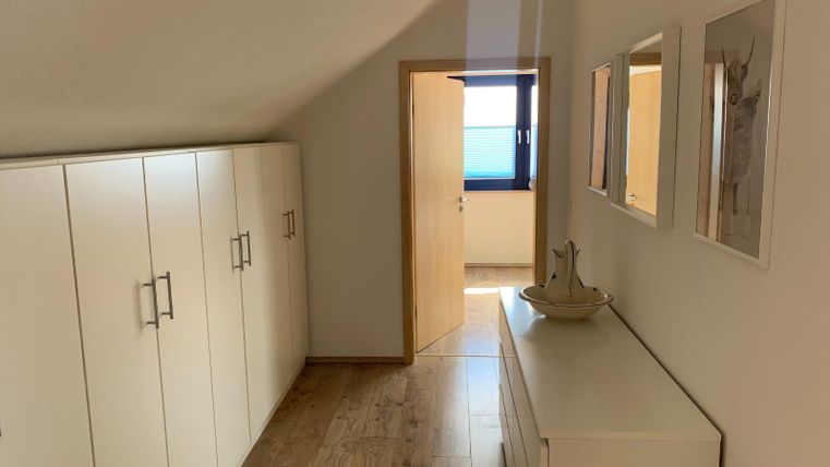Ein heller Flur mit weißen Schränken und einem modernen Sideboard. Die Tür führt zu einem weiteren Raum mit Fenster.