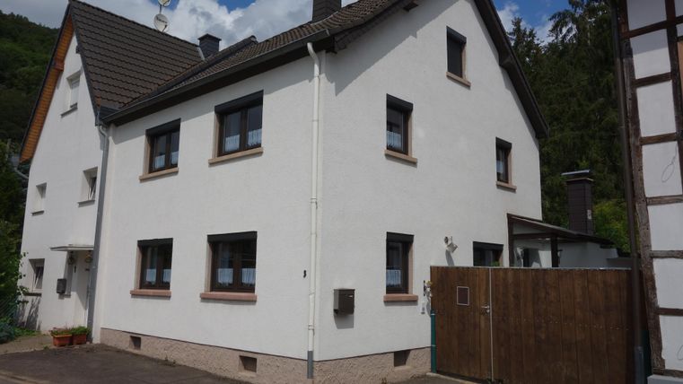 Ein modernes, zweistöckiges Wohnhaus mit weißer Fassade und einem schwarzen Dach. Es befindet sich in einer ruhigen Umgebung mit Bäumen im Hintergrund.
