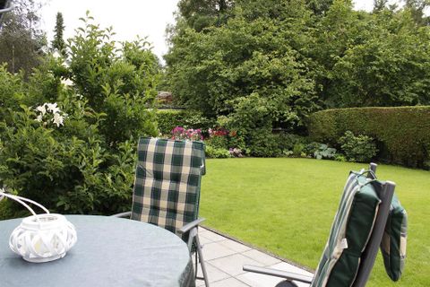 Ein gemütlicher Garten mit grünem Rasen und bunten Blumen. Zwei Stühle und ein Tisch laden zum Entspannen ein.