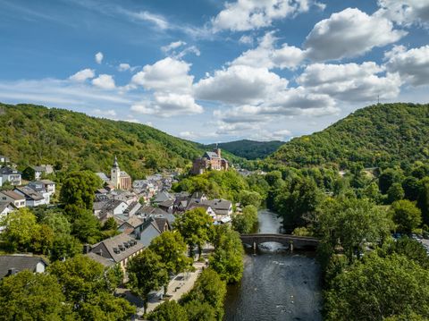 Ein malerisches Tal mit einer kleinen Stadt am Fluss. Grüne Hügel umgeben die sanfte Landschaft unter einem klaren Himmel.