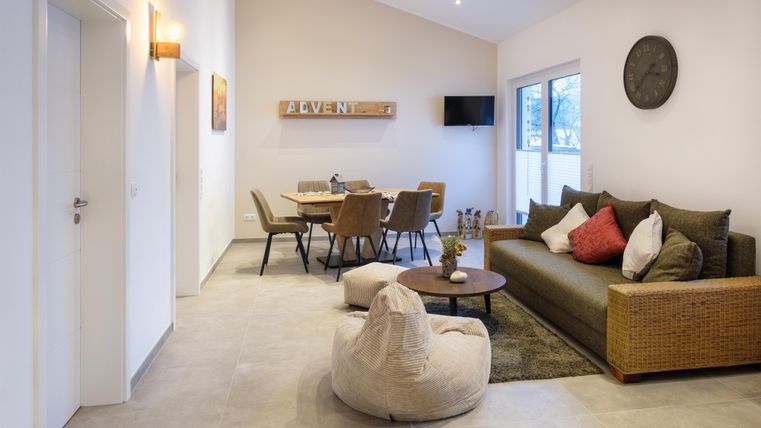 Ein modernes Wohnzimmer mit einem gemütlichen Sofa und einem großen Esstisch. Große Fenster sorgen für viel natürliches Licht.