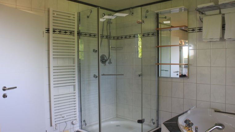 Ein modernes Badezimmer mit einer Dusche und einer Badewanne. Die Wände sind mit hellen Fliesen gestaltet und es gibt einen Spiegel sowie Stauraum.