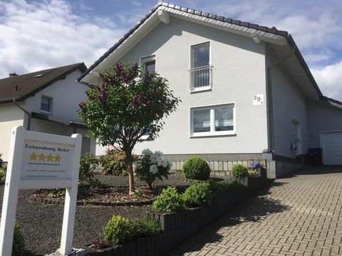 Ein gemütliches Ferienhaus mit einer gepflegten Gartenlandschaft. Der Eingang ist mit einem Schild gekennzeichnet, das die Unterkunft bewirbt.