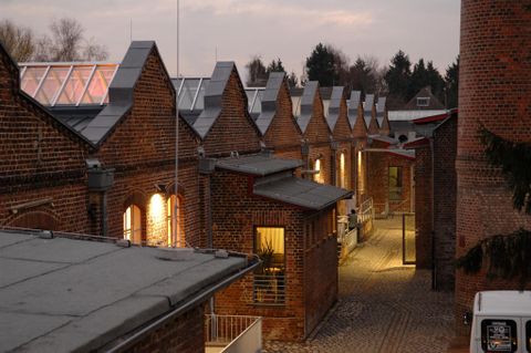 Eine enge Gasse mit Ziegelgebäuden, die symmetrisch angeordnet sind. Die Lichter an den Fenstern verleihen der Szene einen gemütlichen Abendcharakter.