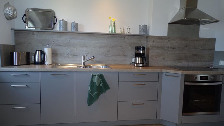 Eine moderne Küche mit grauen Möbeln und einem Holzfußboden. Auf der Arbeitsfläche stehen ein Wasserkocher, eine Kaffeemaschine und einige dekorative Elemente.