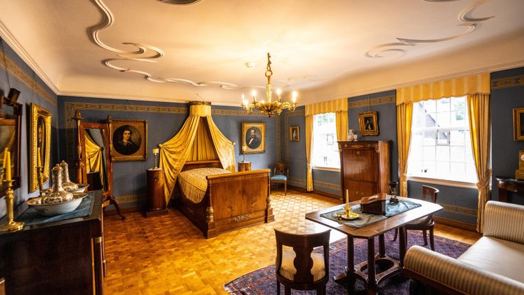 Ein stilvolles Zimmer mit einem großen Bett und eleganter Einrichtung. Die Wände sind mit historischen Bildern geschmückt und das Licht ist warm und einladend.