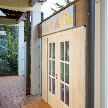 Ein Eingang zu einer Einrichtung namens "Sonnenhalle Pia". Die Tür hat große Fenster und ist aus hellem Holz gefertigt.