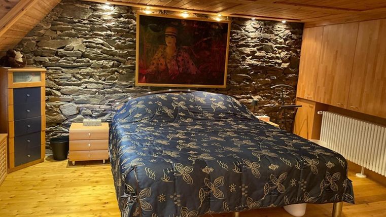 Ein gemütliches Schlafzimmer mit einem großen Bett und einer blauen Bettdecke. Die Wände sind aus Stein, und es gibt Holzmöbel und ein großes Gemälde.