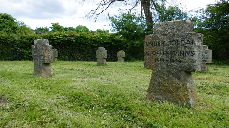 Ein Friedhof mit mehreren Grabsteinen in einer grünen Wiese. Die Grabsteine sind aus Stein und tragen die Inschrift "Unbekannter Soldat".