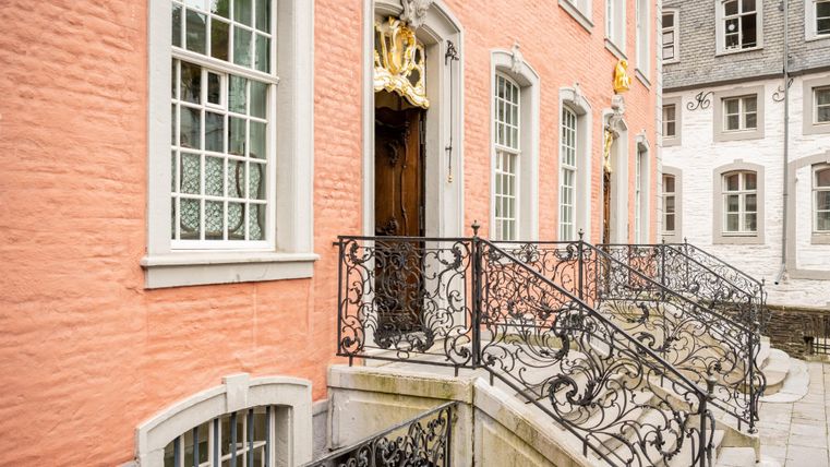Ein elegantes Gebäude mit einer rosa Fassade und historischen Fenster. Die schmiedeeisernen Geländer führen zur Eingangstür.