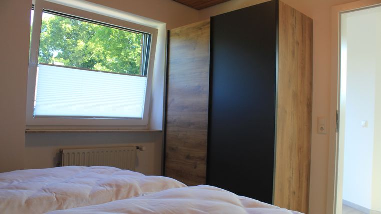 Ein helles Schlafzimmer mit zwei Betten und einem großen Fenster. Ein moderner Schrank steht an der Wand, und die Atmosphäre ist freundlich und einladend.
