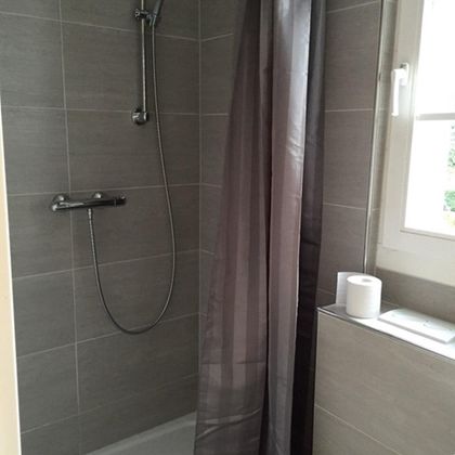 Eine moderne Dusche in einem hellen Badezimmer. Die Wände sind mit grauen Fliesen verkleidet und ein Duschvorhang sorgt für Privatsphäre.