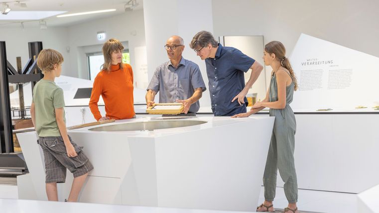 Eine Gruppe von fünf Personen steht um einen Tisch in einem modernen Raum. Sie scheinen ein gemeinsames Projekt oder eine Präsentation zu diskutieren.