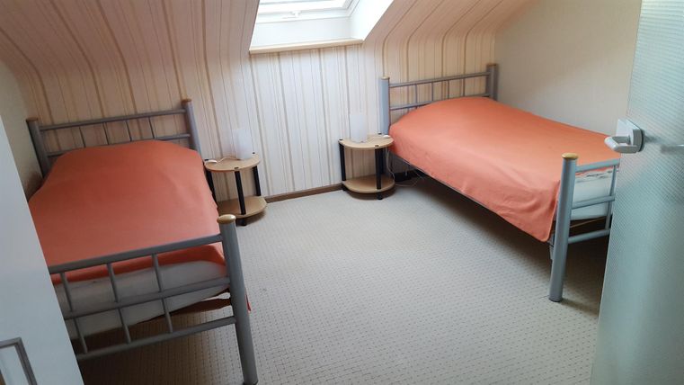 Ein gemütliches Zimmer mit zwei Einzelbetten und orangefarbenen Bettlaken. Das Zimmer hat ein Dachfenster und einen hellen Teppichboden.