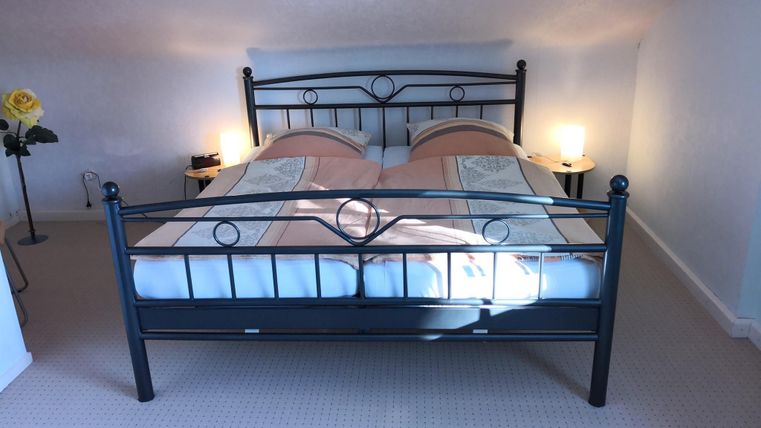 Ein gemütliches Schlafzimmer mit einem Doppelbett und sanfter Beleuchtung. An der Wand steht eine Blume in einer Vase, die dem Raum eine einladende Atmosphäre verleiht.
