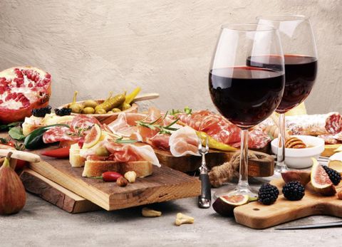 Ein schön gedeckter Tisch mit einer Auswahl an Aufschnitt, Käse, Feigen und Oliven. Dazu zwei Gläser Rotwein und frisches Obst.