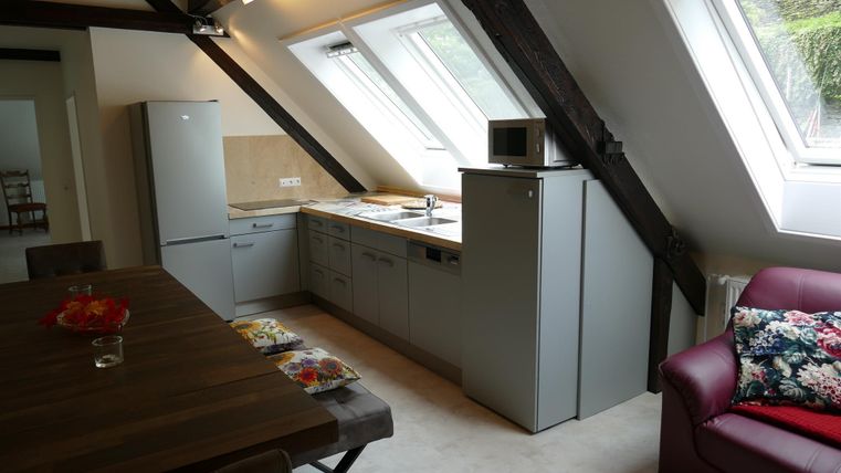 Eine moderne Küche mit grünen Schränken und hellen Wänden. Im Vordergrund steht ein stilvoller Esstisch und ein gemütliches Sofa.
