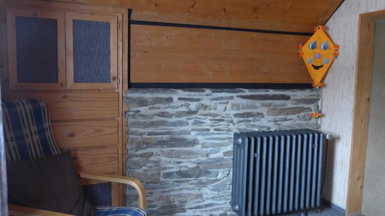 Ein gemütlicher Raum mit einem Sessel und einem Heizkörper. Die Wände bestehen aus Holz und Stein, und eine Kinderfigur ist an der Wand angebracht.