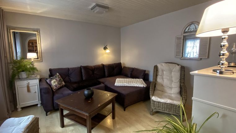Ein gemütliches Wohnzimmer mit einem dunkelbraunen Sofa und einem Tisch. Eine Stehlampe und Pflanzen sorgen für eine einladende Atmosphäre.