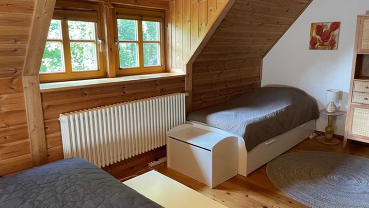 Ein gemütliches Zimmer mit zwei Betten und Holzwänden. Große Fenster sorgen für viel Tageslicht und eine angenehme Atmosphäre.