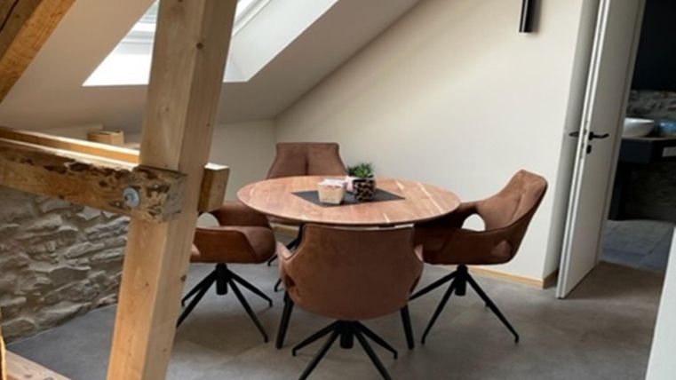 Ein gemütlicher Essbereich mit einem runden Holztisch und vier Stühlen. Große Fenster sorgen für viel Tageslicht und eine angenehme Atmosphäre.