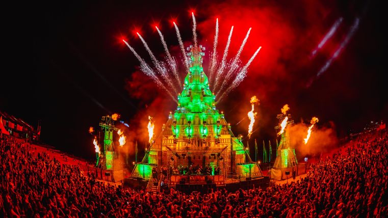 Eine beeindruckende Festivalbühne mit grüner Beleuchtung und Feuerwerk. Die Menge feiert begeistert unter einem spektakulären Nachthimmel.