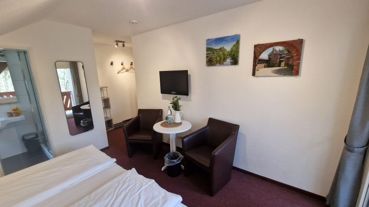 Ein gemütliches Zimmer mit zwei Betten, einem Tisch und zwei Stühlen. An der Wand hängen Bilder, und es gibt einen Fernseher.