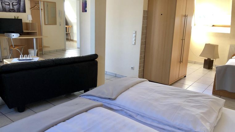 Ein gemütliches Zimmer mit zwei Betten, einem schwarzen Sofa und einem Kleiderschrank. Der Raum ist hell und freundlich eingerichtet.