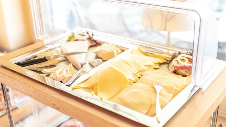 Ein Buffet mit verschiedenen Käsesorten und Wurst. Die kunstvoll angerichteten Produkte sind unter einer Glasabdeckung präsentiert.