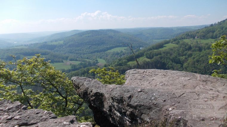 Eine beeindruckende Aussicht von einem Felsen auf grüne Hügel und sanfte Landschaften. Der Himmel ist klar und strahlend blau.