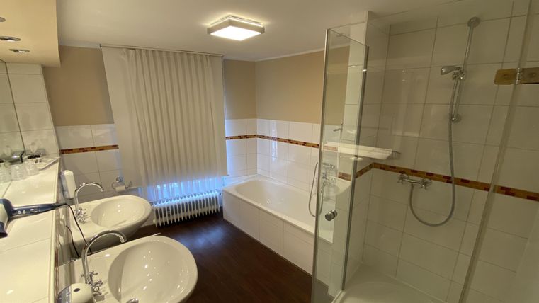 Ein modernes Badezimmer mit Dusche und Badewanne. Es verfügt über helle Farben und zwei Waschbecken.