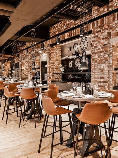 Ein modernes Restaurant mit Holzfußboden und gemauerten Wänden. Tische sind mit eleganten Stühlen und Besteck dekoriert.