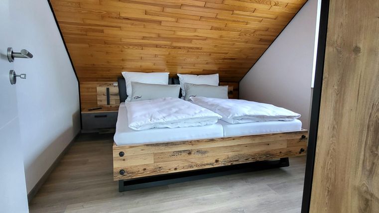 Ein gemütliches Schlafzimmer mit Dachschräge. Es verfügt über ein Doppelbett aus Holz und einen warmen Holzboden.