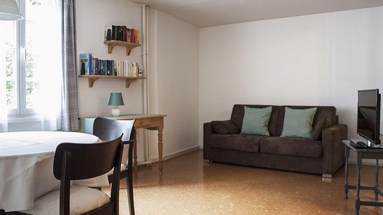 Ein modernes Wohnzimmer mit einem gemütlichen Sofa und einem Tisch. Bücherregale und ein Fernseher ergänzen die Einrichtung.