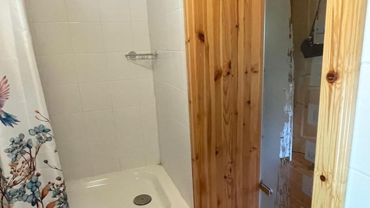 Eine einfache Dusche mit weißen Fliesen und einem holzverkleideten Eingangsbereich. Der Duschvorhang zeigt ein florales Design.