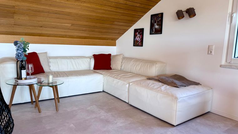 Ein gemütliches Wohnzimmer mit einer weißen L-Form-Couch und roten Kissen. Ein Beistelltisch mit Glas und zwei Gläsern steht in der Mitte.