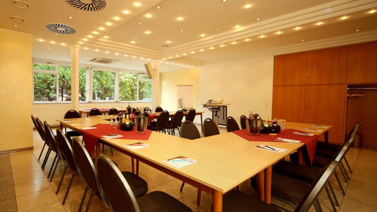 Ein eleganter Besprechungsraum mit einem großen Tisch und mehreren Stühlen. Der Raum ist gut beleuchtet und hat Fenster, die für Tageslicht sorgen.