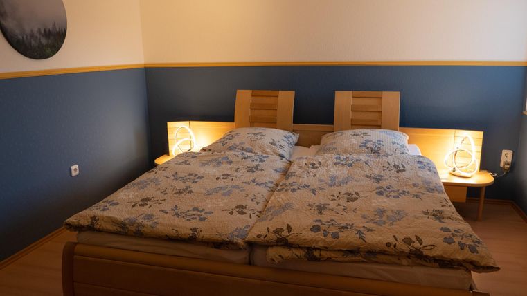 Ein gemütliches Schlafzimmer mit einem Doppelbett und blumigen Bettdecken. Die Wände sind in Blau und Gelb gestrichen, und es gibt Nachttische mit Lampe.