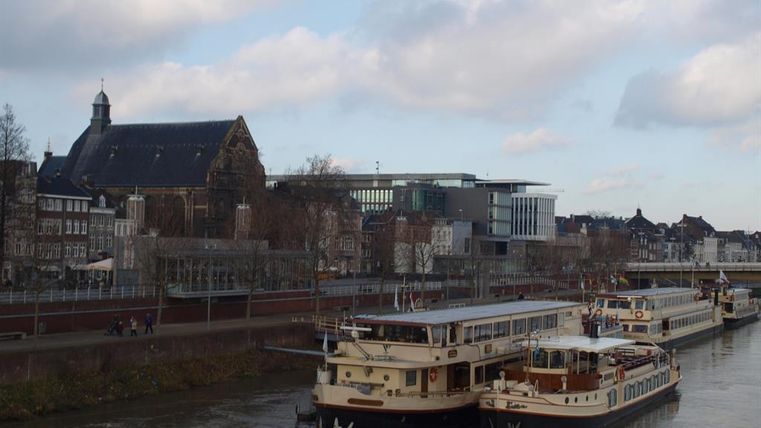 Eine Ansicht des Wassers mit mehreren Booten im Vordergrund. Im Hintergrund sind Gebäude und eine Kirche zu sehen, unter einem bewölkten Himmel.