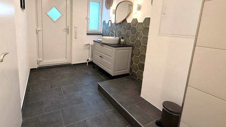 Ein moderner Flur mit grauen Fliesen, einem hellen Eingangsbereich und einer stilvollen Wandverkleidung aus Hexagonfliesen. Der Raum ist gut beleuchtet und hübsch dekoriert.