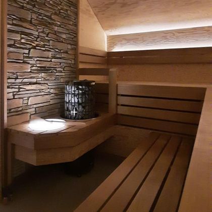 Ein entspannender Sauna-Raum mit Holzbänken und einer Steinwand. Sanftes Licht sorgt für eine angenehme Atmosphäre.