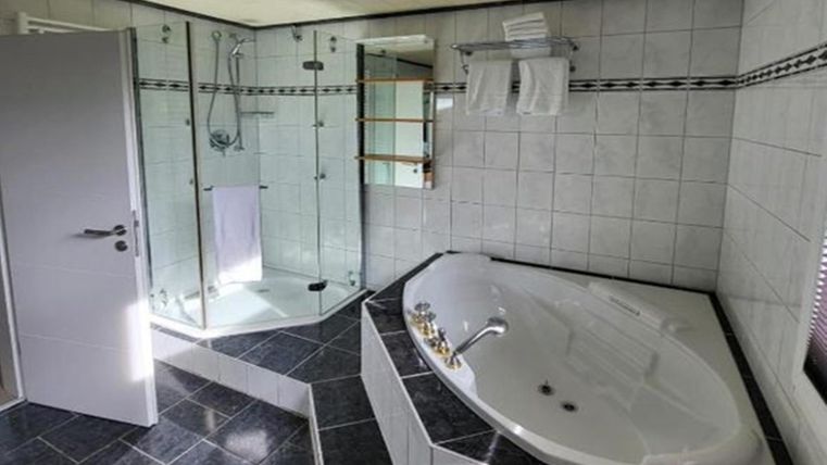 Ein modernes Badezimmer mit einer Badewanne und einer separaten Dusche. Die Wände sind hell gefliest, und es gibt handtücher in einer praktischen Halterung.
