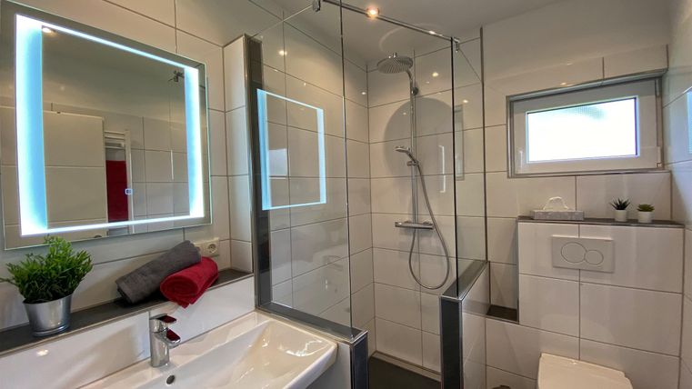 Ein modernes Badezimmer mit einem Glasduschbereich und einem eleganten Waschbecken. Große Spiegel mit LED-Beleuchtung und helle Fliesen schaffen eine ruhige Atmosphäre.