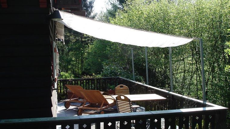 Eine gemütliche Terrasse mit Liegestühlen und einem Tisch. Im Hintergrund ist üppiges Grün und Bäume zu sehen.