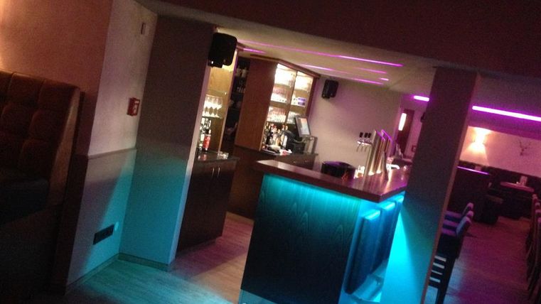 Eine stilvolle Bar mit einem beleuchteten Bartresen. Der Raum hat gemütliche Sitzgelegenheiten und sanfte, farbige Beleuchtung.