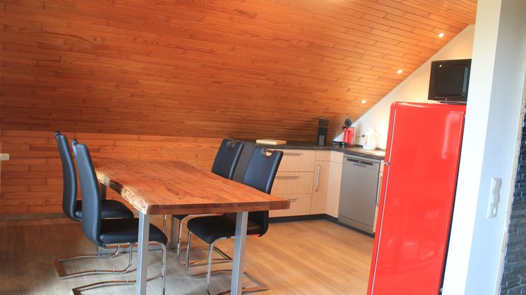 Eine moderne Küche mit Holzverkleidung und einem großen Esstisch. Der rote Kühlschrank und die stilvollen Stühle setzen einen auffälligen Akzent.