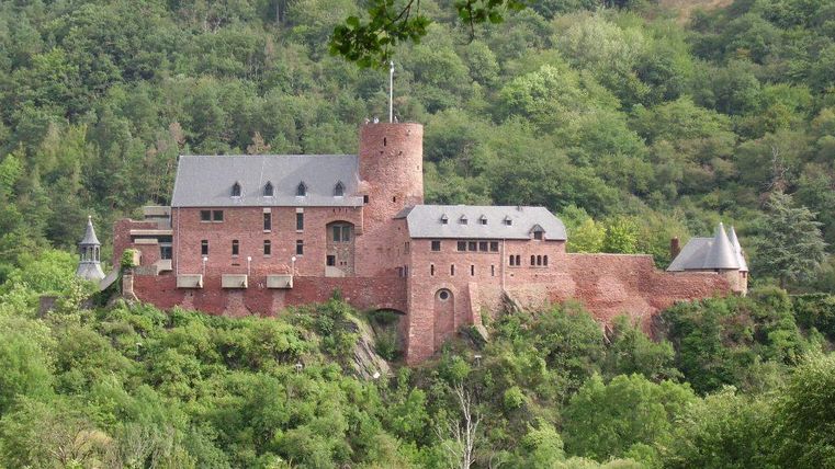 Eine beeindruckende Burg inmitten grüner Hügel. Die charakteristischen roten Backsteinwände und der markante Turm prägen die Szenerie.