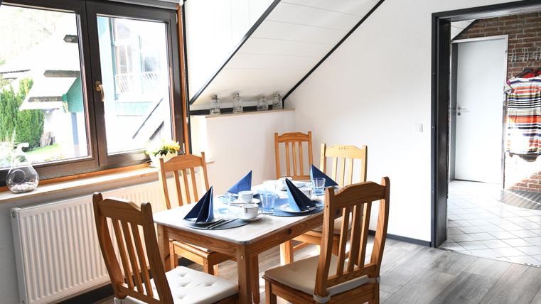 Ein helles Esszimmer mit einem Tisch und vier Stühlen. Der Tisch ist festlich gedeckt mit blauen Servietten und Geschirr.