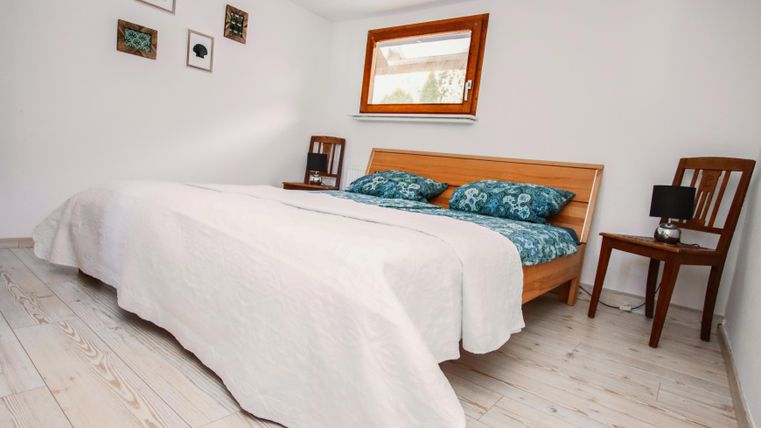 Ein helles Schlafzimmer mit einem Doppelbett und gemütlichen Kissen. Neben dem Bett steht ein Holzstuhl und ein Nachttisch mit einer Lampe.